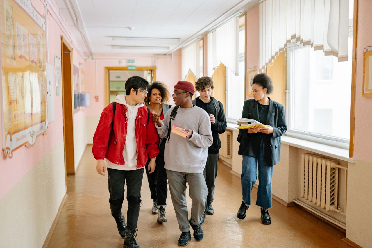 About A diverse group of college students walking and conversing in a university hallway.